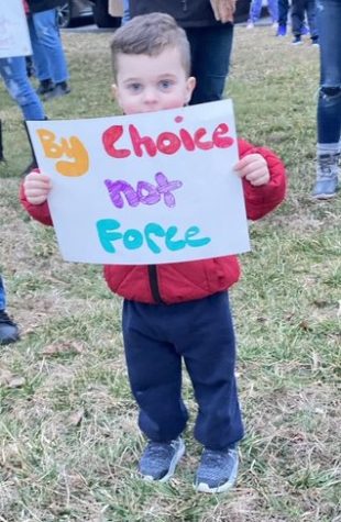 A young child timidly carries a sign at an anti-masking protest. Photo by Mr. Allen.